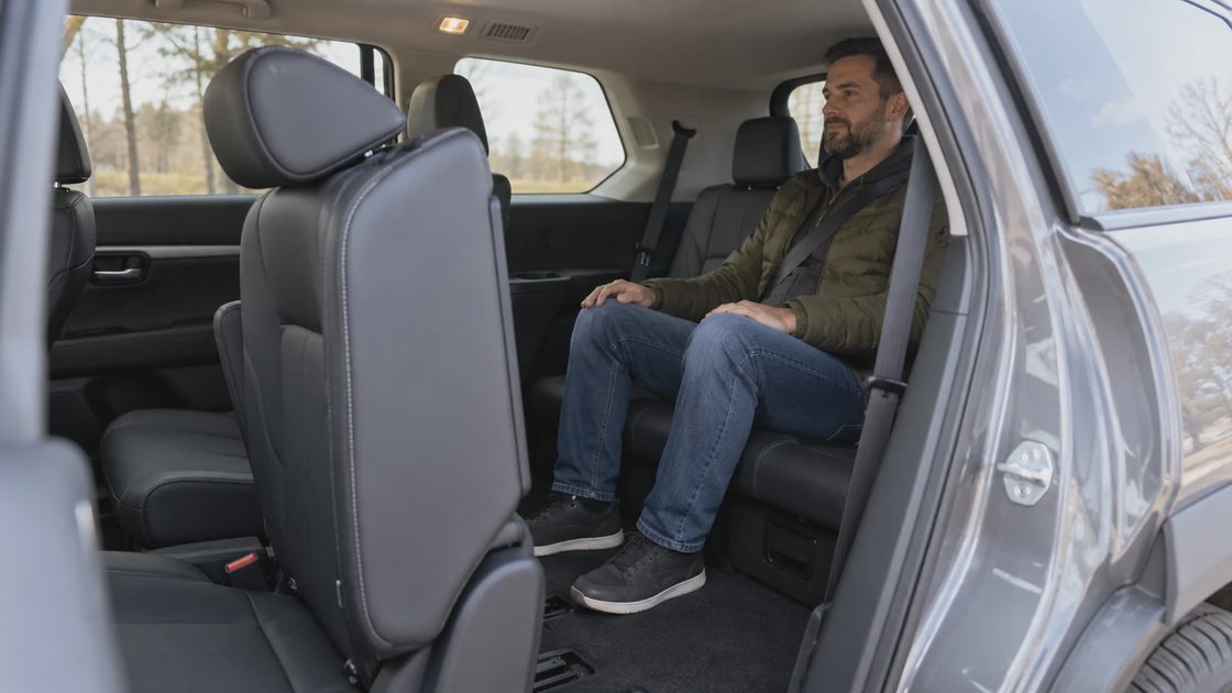 An adult checking third-row access in a parked crossover.